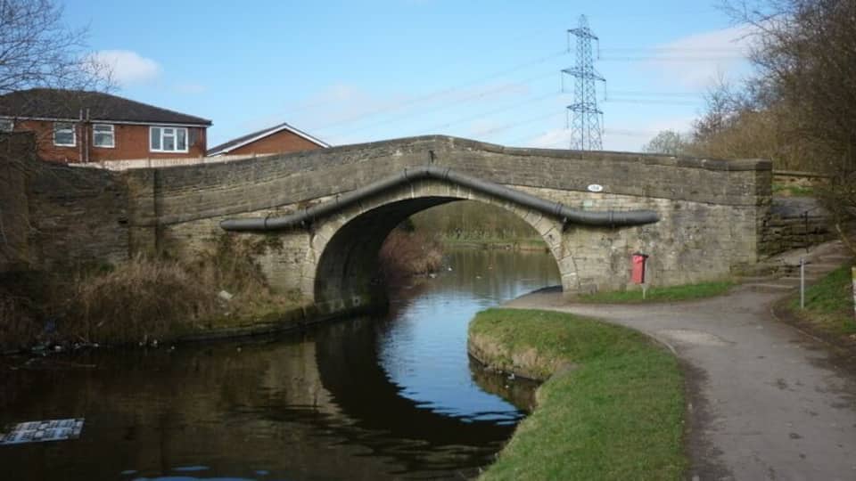 A stone bridge over a canal with a grassy bank and a path on the right.