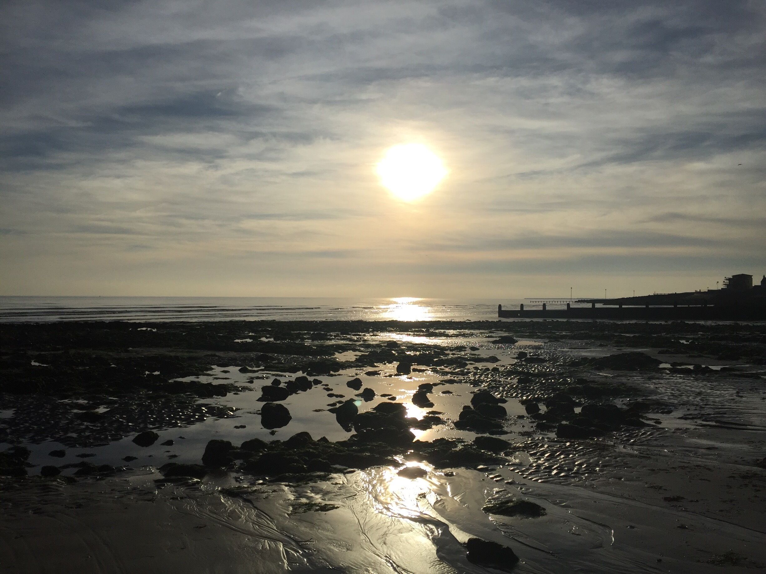 A beach with rocks and a pier in the background.