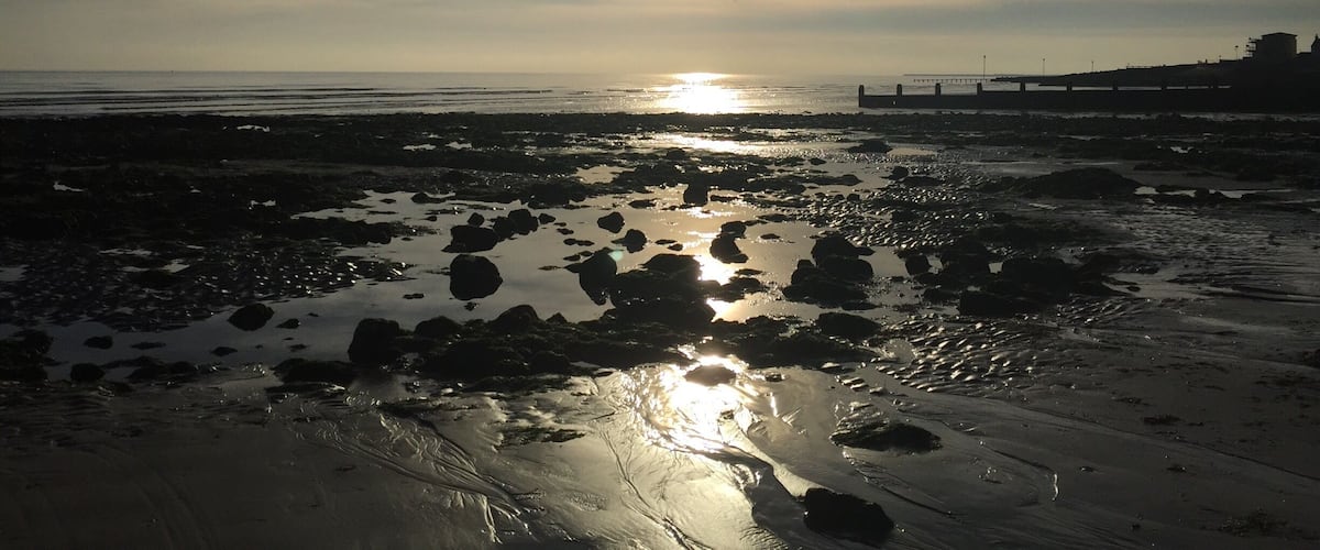 A beach with rocks and a pier in the background.
