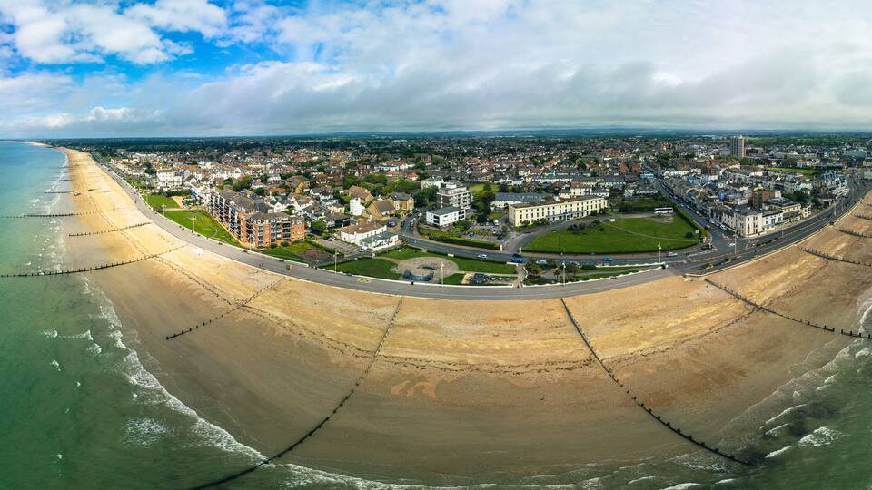 An aerial view of a coastal city with a curved beach, a pier, and a mix of residential and commercial buildings.