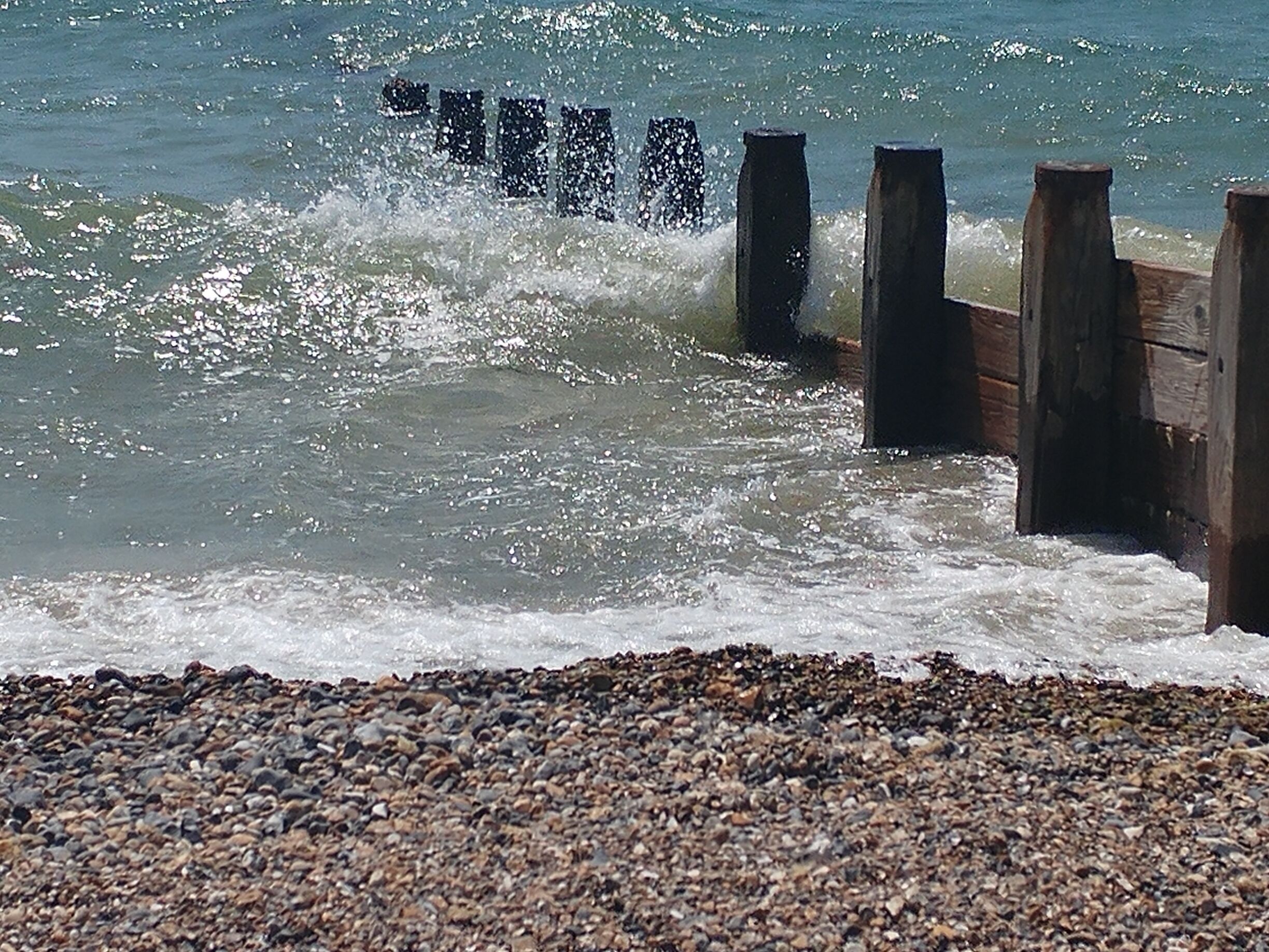 A wooden breakwater with waves crashing against it.