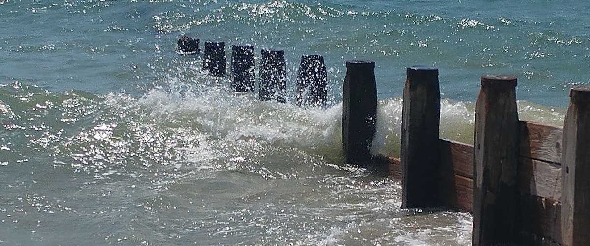 A wooden breakwater with waves crashing against it.