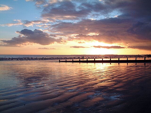 A sunset over a beach with a wooden pier extending into the water.
