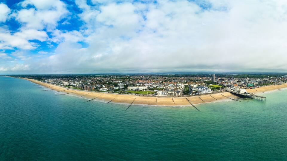 An aerial view of a coastal city with a beach, pier, and dense urban area.