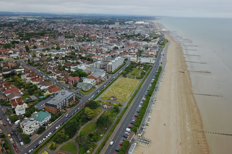 Vista aérea de un pueblo costero con playa, zonas residenciales y un estadio grande.