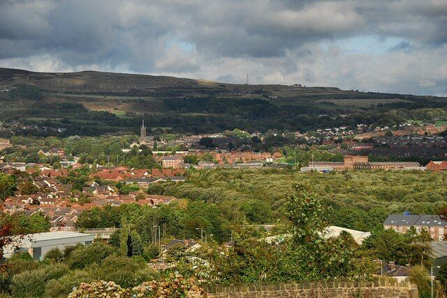 A town with red-roofed houses, a church spire, and rolling hills in the background.