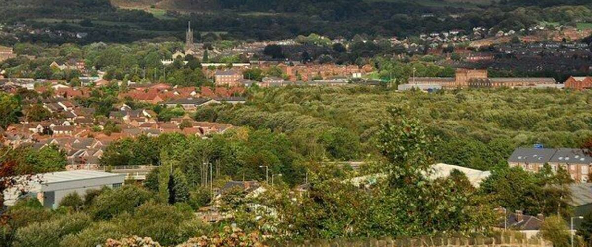 A town with red-roofed houses, a church spire, and rolling hills in the background.