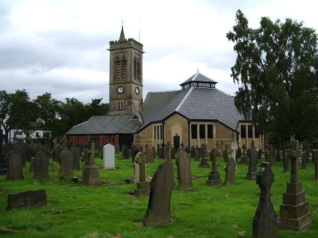 A church with a clock tower and a cemetery with gravestones.