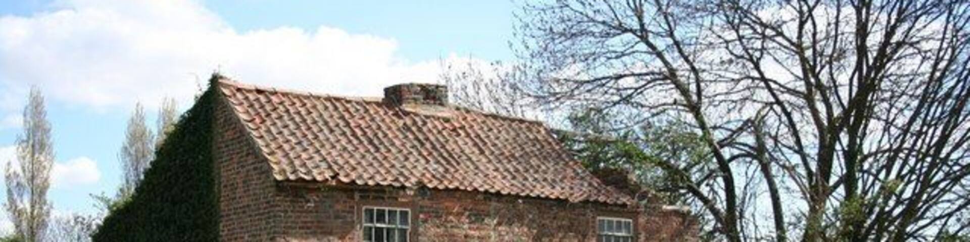 A brick house with a tiled roof, surrounded by grass and trees.