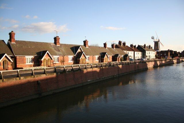 A canal with brick houses along its banks and a windmill in the background.
