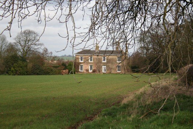 A large brick house with multiple windows, surrounded by a grassy field and trees.