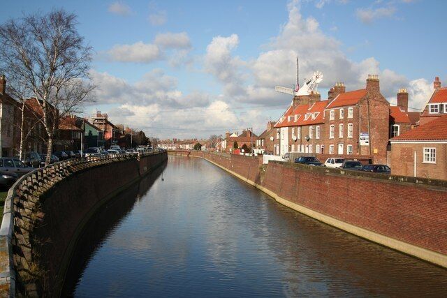 A canal with brick buildings and a windmill on the right.
