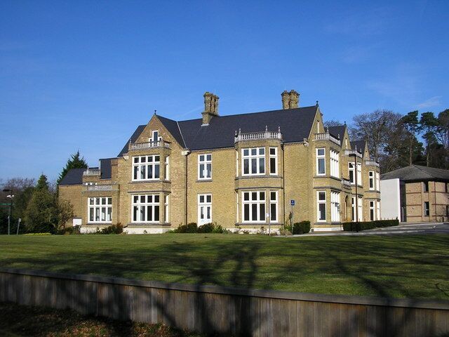 A large, two-story stone building with a symmetrical facade, multiple windows, and a prominent chimney.