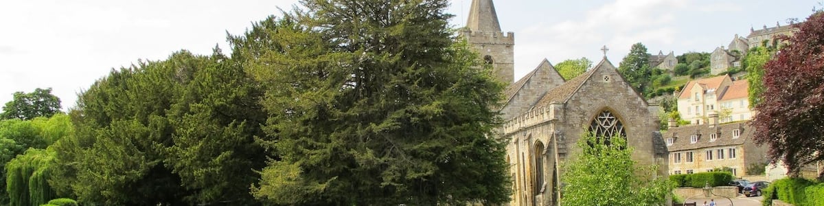 Eine historische Kirche mit einem hohen Turm, umgeben von üppiger Vegetation und einem Fluss.