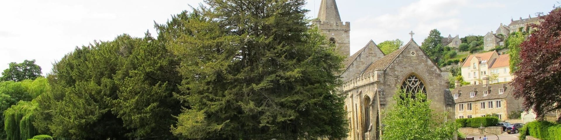 A historic church with a tall spire, surrounded by lush greenery and a river.