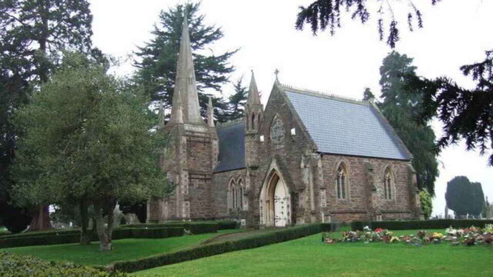 A church with a tall spire, surrounded by a well-manicured lawn and trees.