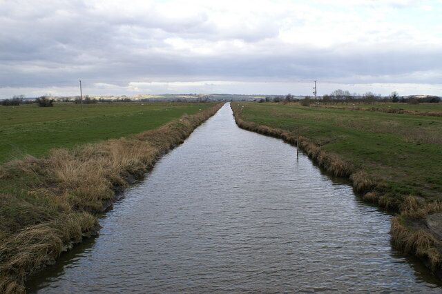 A narrow waterway flanked by grassy fields under a cloudy sky.
