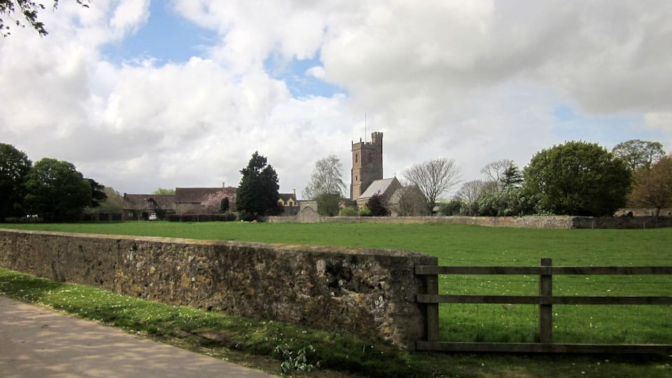 A rural landscape with a stone wall, a wooden fence, and a church with a tall tower.