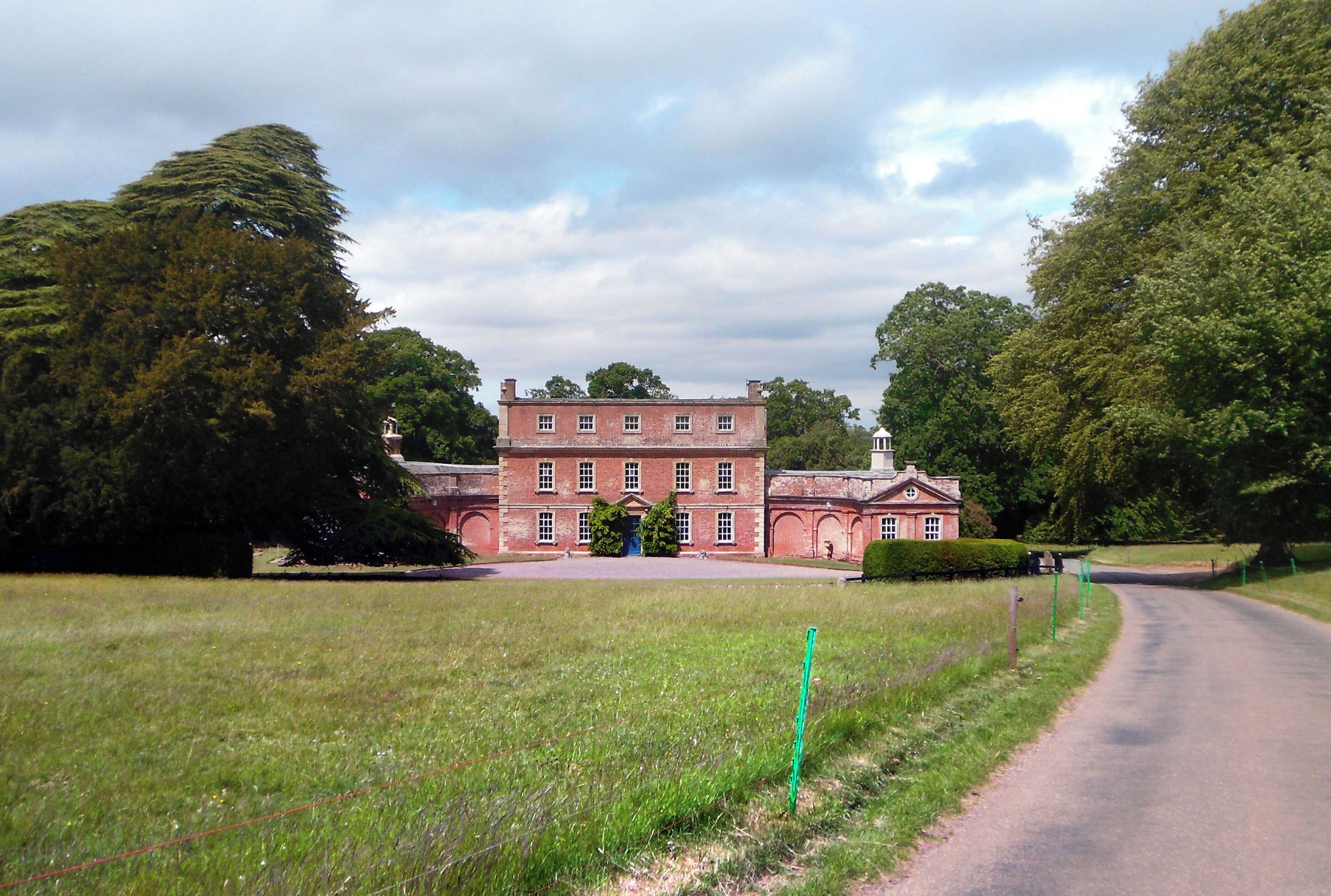 A large red brick building with a symmetrical facade, surrounded by lush green trees and a grassy field.