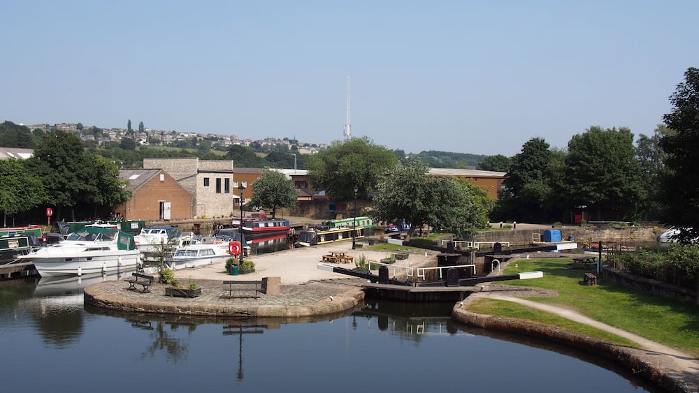 A calm harbor with boats docked, a small island with a dock, and buildings in the background.