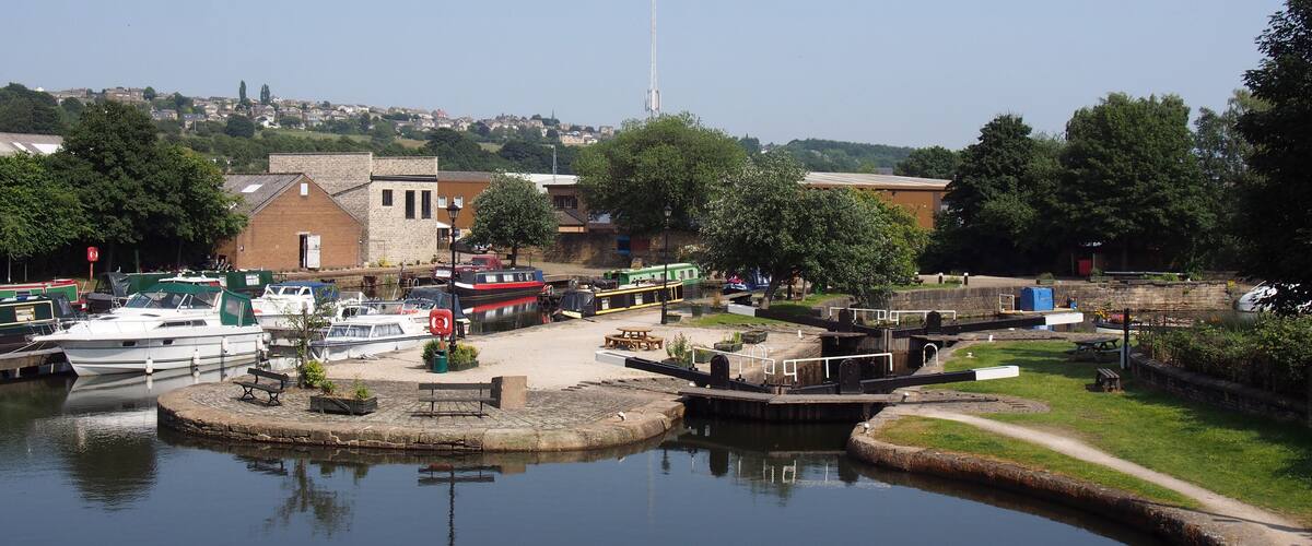 A calm harbor with boats docked, a small island with a dock, and buildings in the background.