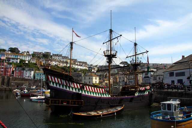 A historic ship docked in a harbor with colorful buildings in the background.