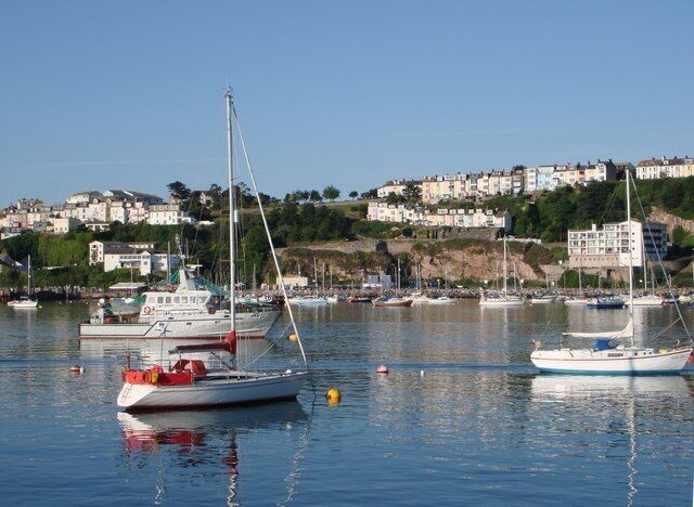 A harbor with boats, a lighthouse, and a hillside with buildings.