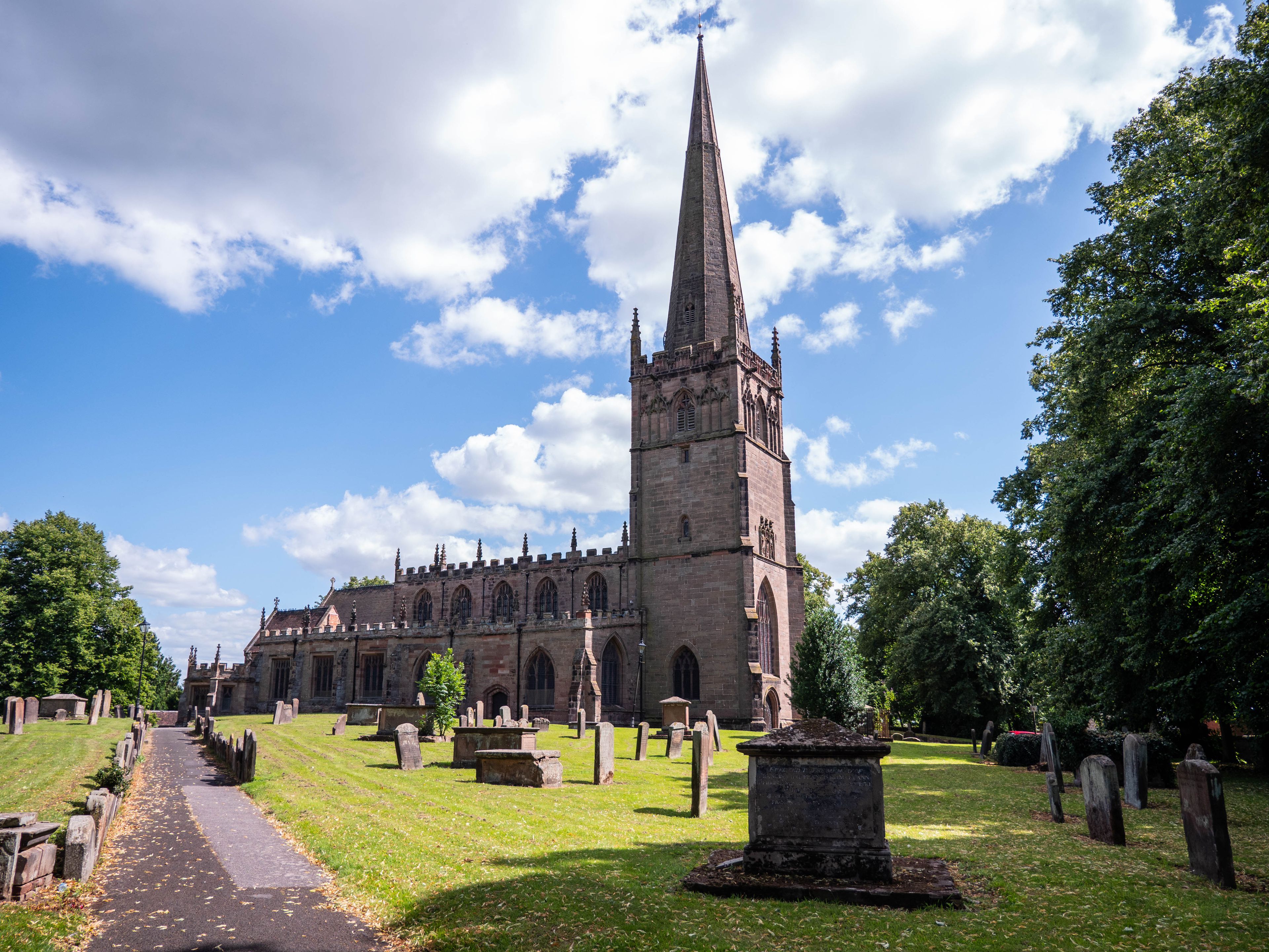 En historisk kirke med et højt spir, omgivet af en kirkegård med gravsten.