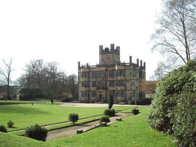 A large, historic building with a tower, surrounded by well-maintained lawns and trees.