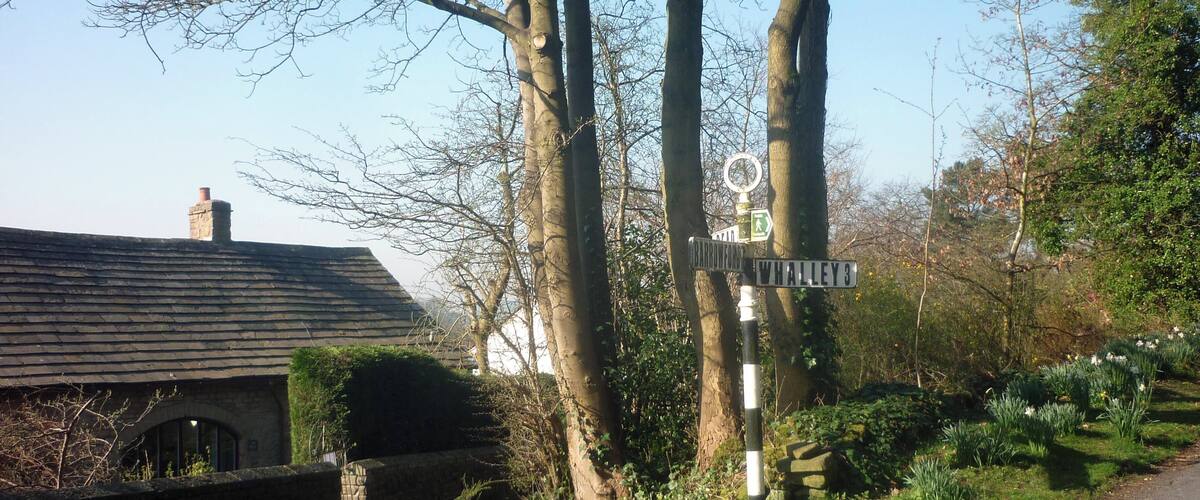 A rural road with a directional signpost, a stone house, and blooming daffodils.