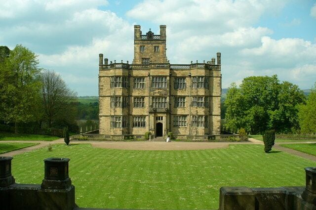 A large, historic stone building with a central tower, surrounded by a well-maintained lawn and trees.