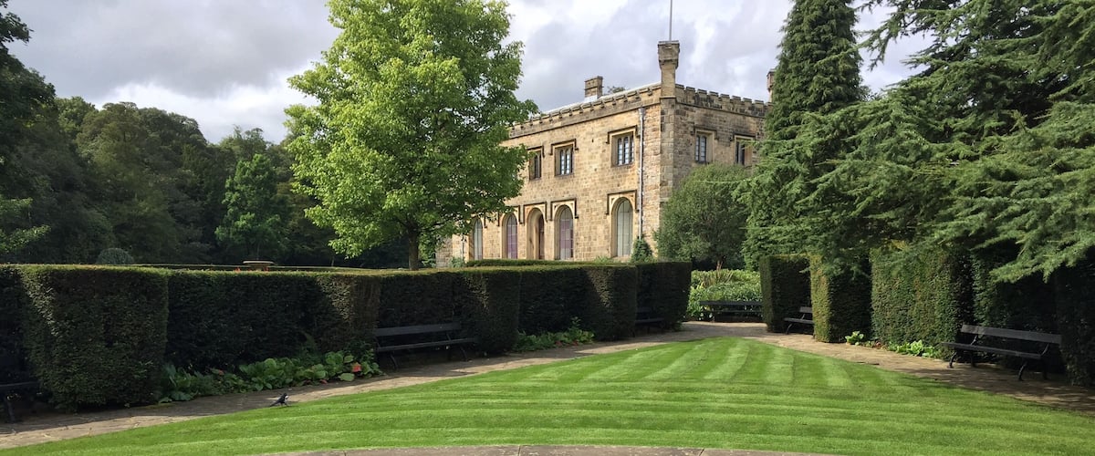 A well-manicured lawn, a pond, and a historic building in the background.