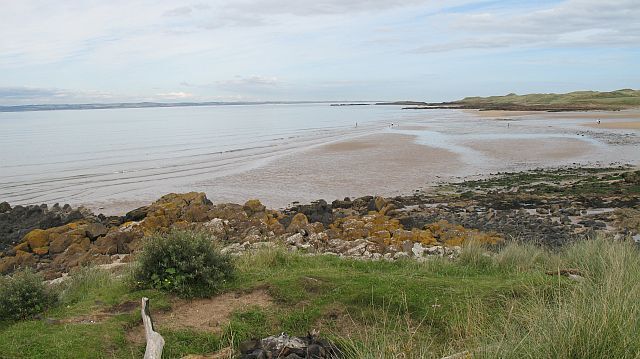 A coastal beach with rocky outcrops and calm waters.