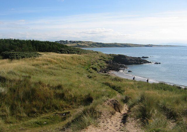A coastal landscape with grassy dunes, a sandy beach, and a calm sea.