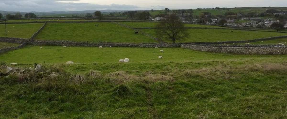 A rural landscape with green fields, stone walls, and a distant village.