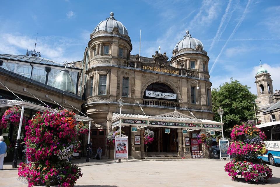 An ornate building with domed architecture, labeled "Opera House," and signs for "Coffee Morning," "Upper Circle," "Dress Circle and Stalls," and "Private Boxes."