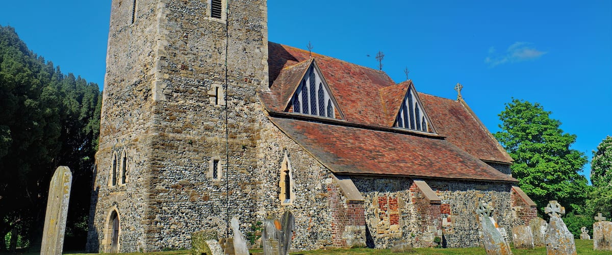 A historic stone church with a bell tower and a cemetery in front.
