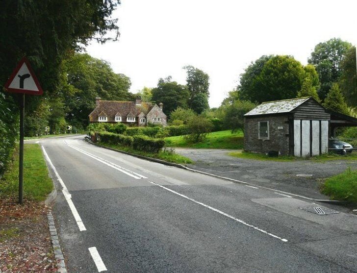 A rural road with a sharp bend, a small building, and a house in the background.