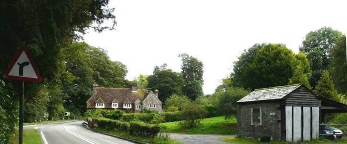 A rural road with a sharp bend, a small building, and a house in the background.