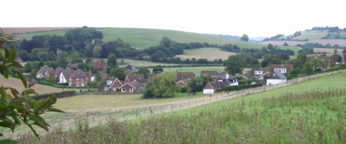 A rural landscape with rolling hills, a small village with houses, and a field in the foreground.