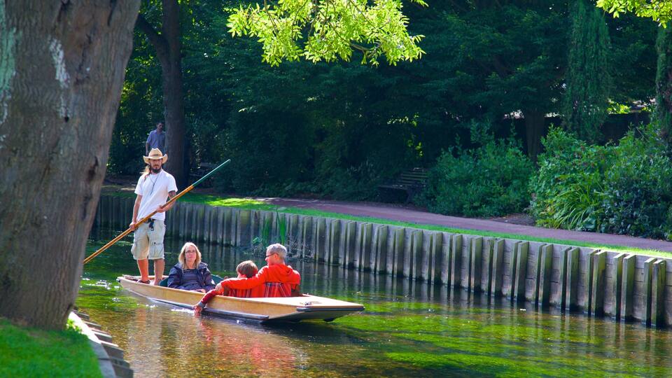 A narrow waterway with a wooden boat carrying passengers, surrounded by lush greenery and a wooden fence.
