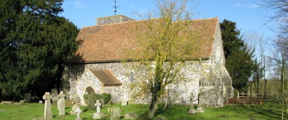 A stone church with a tiled roof, surrounded by a cemetery with headstones.