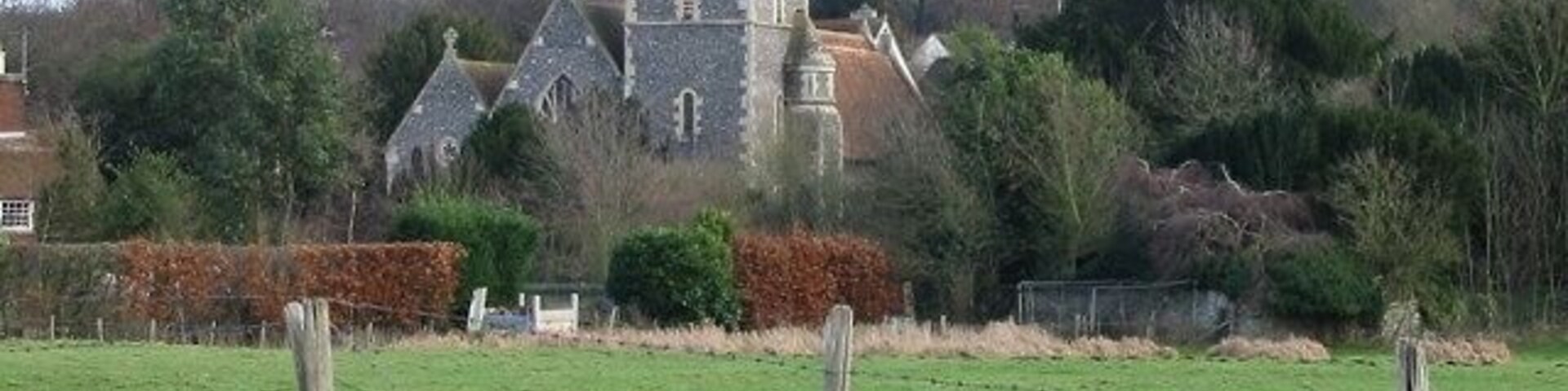 Una iglesia con un campanario alto, rodeada por un campo verde y una valla.