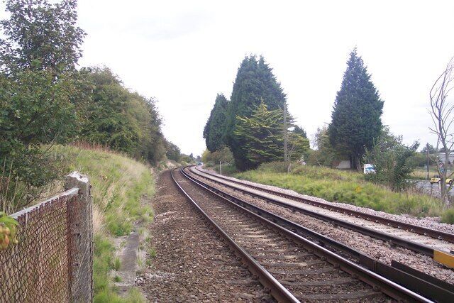 Railway tracks curving through a rural area with trees and a fence on the left.