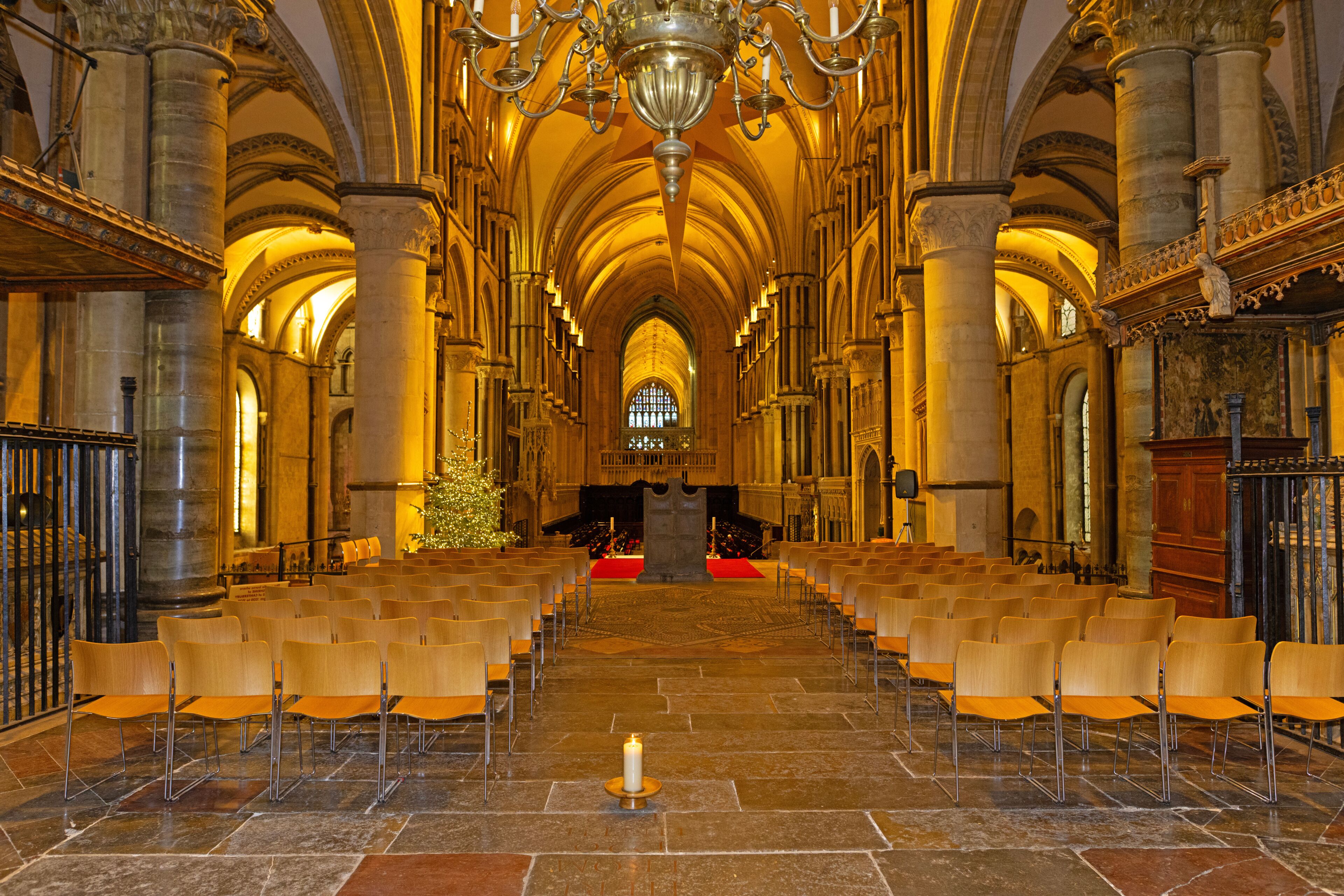 Interior de uma catedral com fileiras de cadeiras, um candelabro e um pinheiro de Natal.