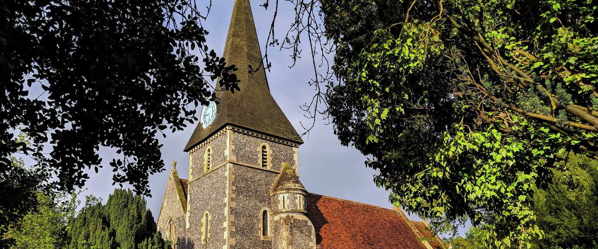 A church with a tall spire, stone walls, and a graveyard with headstones.
