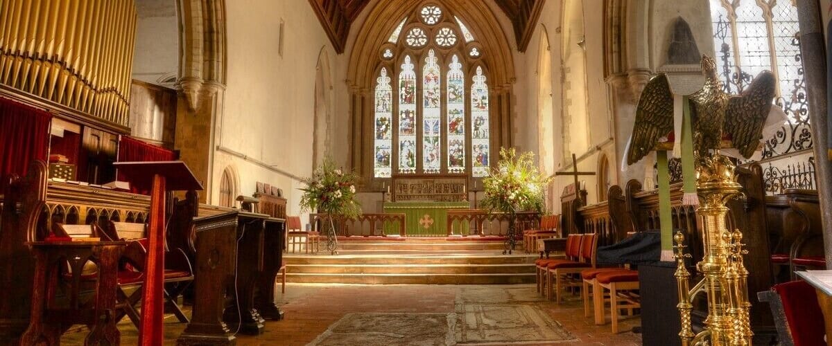 A church interior with a wooden ceiling, stained glass windows, and a pipe organ.