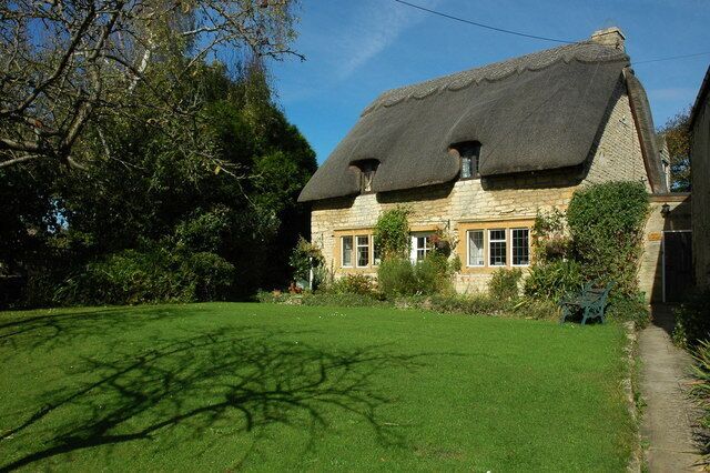 A thatched-roof house with a well-maintained lawn and surrounding trees.