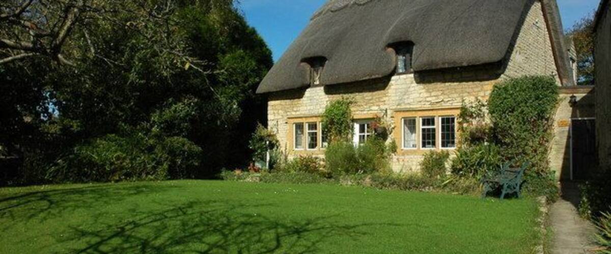 A thatched-roof house with a well-maintained lawn and surrounding trees.