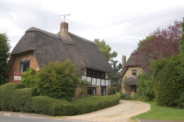 A thatched-roof house with a sign indicating it's for sale.
